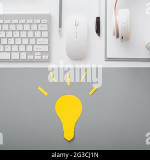 Yellow light bulb idea insight concept on student desktop with keyboard pc computer mouse headphones and white suppliers in workspace on gray table Stock Photo