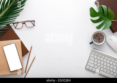 Modern work space with computer keyboard and office supplies. Empty mobile phone mockup on white table with tropical palm leaves. Frame Flat lay Stock Photo