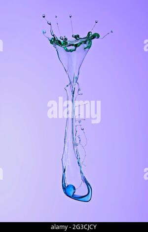 A vessel shape created when two colored water drops from above collide with a pressure spout from below to form an interesting shape against a purple Stock Photo