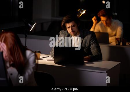 Group of young confident business colleagues working on startup project at night. tired sleepy Caucasian Business People with pc computer working late Stock Photo