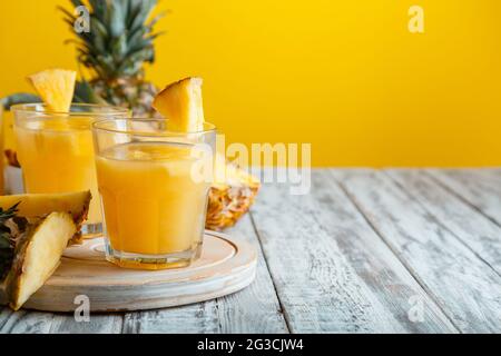 Tasty pineapple juice in glass with ingredients on white wooden table with yellow summer background. Fresh natural pineapple juice cocktail and juice Stock Photo