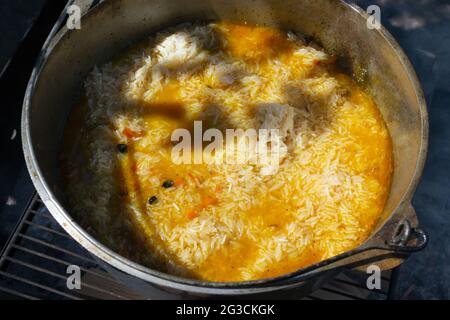 Cooking pilaf in a cauldron over a fire. Rice with meat and vegetables are stewed in a zervak for a while. Traditional oriental cuisine concept. Stock Photo