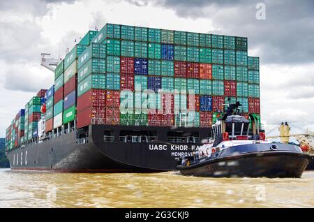 Huge panamax container cargo ship in the panama canal aided by a tug boat