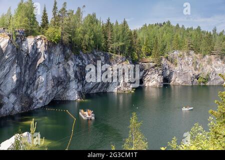 Ruskeala, Russia - June 12, 2021: Karelian landscape with former marble quarry filled with groundwater. Tourists are in boats and on a rocky coast Stock Photo