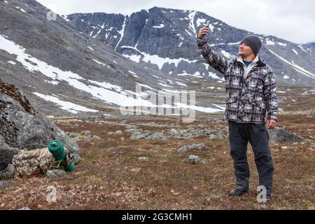 Backpack traveler trying to call with phone with weak signal, rising up his hand with smartphone, Caucasian man Stock Photo