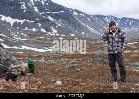 Backpack traveler calls with mobile phone with weak signal, speaks with his smartphone Stock Photo