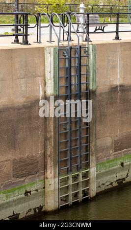 Tall ladder on the side of a concrete wall with water from the canal down below on a sunny day Stock Photo
