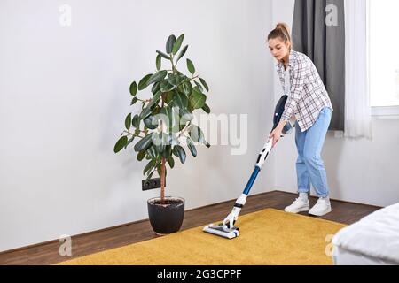 Caucasian woman wearing casual clothes cleaning house floor in living room using modern vacuum cleaner during Staying at home using free time about da Stock Photo