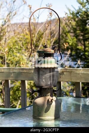 very old rusty and dusty gas lamp for outdoor on a glass table next to a fence on a sunny day Stock Photo