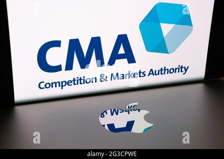 Apple logo on macbook surface and blurred UK CMA Competition and Markets Authority logo seen on the smartphone screen.  Concept. Stafford, United King Stock Photo