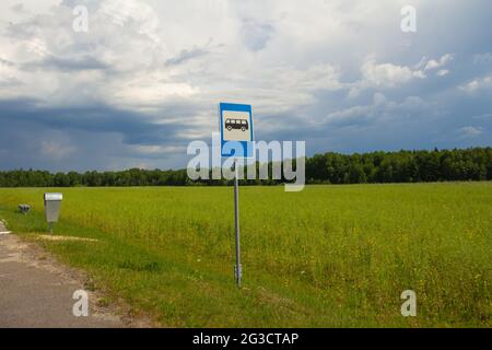 Bus stop sign on a background of blue cloudy sky, green field and forest on a summer sunny day. Stock Photo