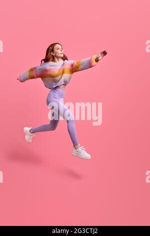 Portrait of happy joyous woman jumping or flying, hurry running to her dream, looking at side inspired. indoor studio shot isolated on pink studio bac Stock Photo