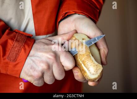 Close up on a masculine hands cutting the peel off a potato with a sharp knife Stock Photo