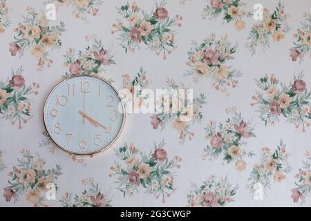 rose gold round shape clock mounted on a wall with floral wallpaper Stock Photo