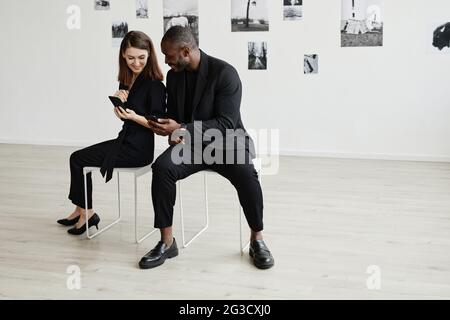 Minimal high angle portrait of elegant mixed-race couple wearing black while using smartphones in modern art gallery, copy space Stock Photo