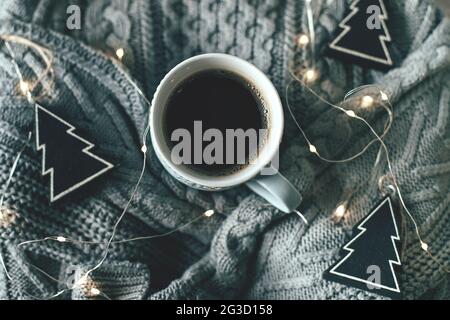 Cozy, mood, lifestile, stilllife concept. Mug of coffee, sweater, garland lights on knitted sweaters Stock Photo