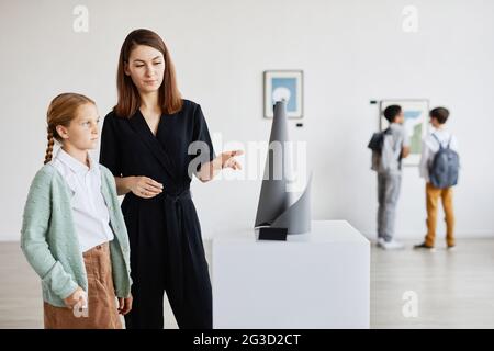 Portrait of mother and daughter looking at sculptures in modern art gallery, copy space Stock Photo