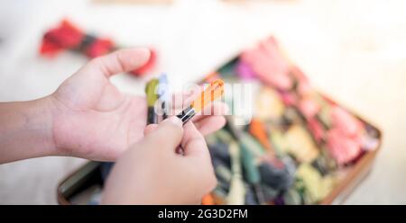 Close up hands of tailor woman holding many threads of different colors on table and prepare to use with white cotton and frame wood. For hobby. Stock Photo