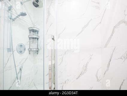 Shower in a modern bathroom with marble walls and clear glass in the front and removable shower head with metal wires and pipes Stock Photo