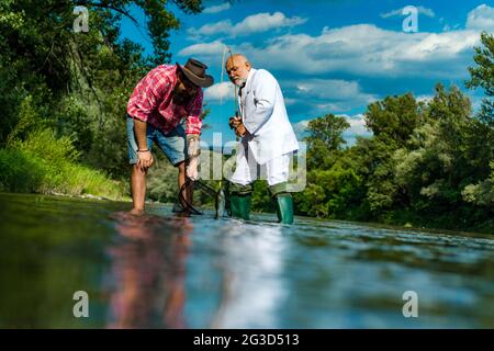 Father and adult son fishing lakeside. Having a good time. Fisher fishing equipment. Giving your hobby. Master baiter. I am happiest man. Angler Stock Photo