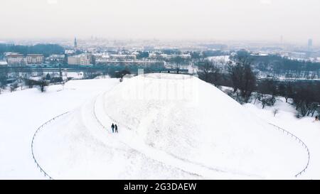 Panoramic view of the Krakus Mound (Kopiec Krakusa) also called Krak Mound. A tumulus located in the Podgórze district of Kraków, Poland. Tourists can be seen standing. Whole area covered with snow.  Stock Photo