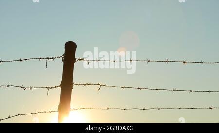 Setting sun behind a fence of barbed wire Stock Photo - Alamy