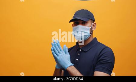 Young Indian man wearing mask and gloves taking precautions. Dressed in blue polo and blue cap. Concept of Pandemic. Covid 19. Delivery boy following SOPs.  Stock Photo