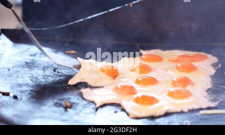 Multiple cracked eggs frying on a bbq grill plate. Egg yolks and whites being fried or cooked in large quantities on a barbecue griller. Community fun Stock Photo