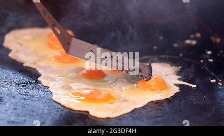 A close up of multiple eggs being cooked on a barbecue or grill plate. Egg yolk being pierced or opped by bbq slide. Fried eggs getting cooked. Stock Photo