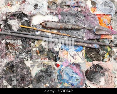 A full view of a artists painting palette loaded with rich thick wet oil paint, brushes and palette modeling knife. Isolated on a white background Stock Photo