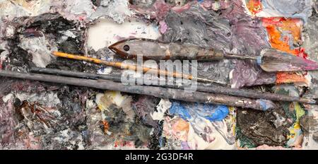 A wide close up view of a artists painting palette loaded with rich thick wet oil paint, brushes and palette modeling knife. Stock Photo