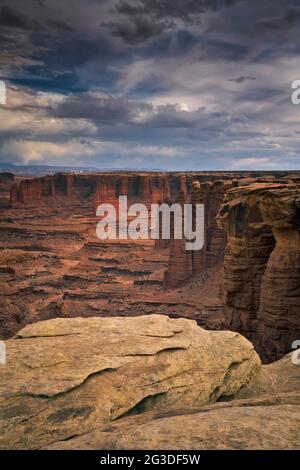 Evening light glow on the towering sandstone spires of Monument Basin as storm clouds gather over this remote White Rim Road view in Utah’s Canyonland Stock Photo