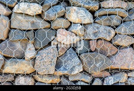 Stone wall with metal grid as background. Rock texture in metal grid. Gabion net Stock Photo