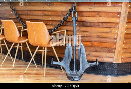 Black metal anchor and anchor chain next to a wooden wall Stock Photo