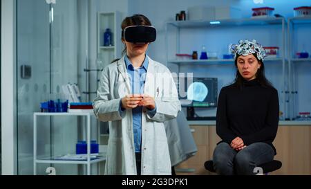 Laboratory doctor experiencing virtual reality using vr goggles in medical neurological research lab. Physician therapist using medical innovation equipment device glasses, analysing brain scan Stock Photo