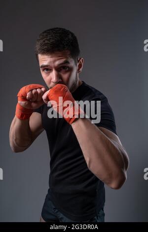 Young boxer with red bandages on hands posing in orthodox stance Stock Photo