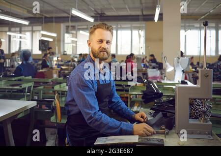 Smiling male shoemaker makes a new pair of leather shoes at a modern shoe factory. Stock Photo