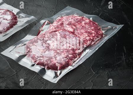 Raw fresh beef burgers minced meat in plastic tray set, on black stone background, with copy space for text Stock Photo