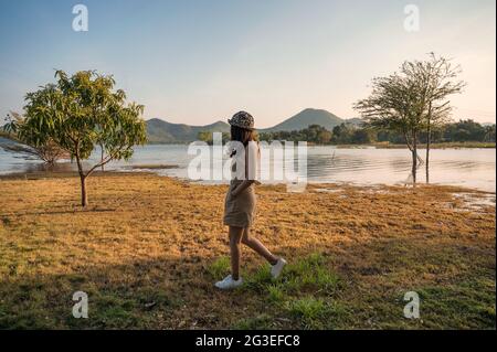 Young asian woman walking on side of reservoir and mountain view in the evening Stock Photo