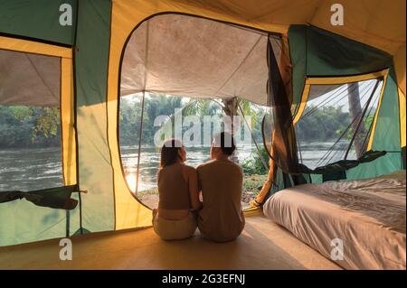 Young asian couple relaxing inside a tent on campsite in natural park at the evening Stock Photo