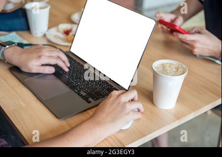 Freelance man working with empty display laptop and coffee cup on wooden table in cafe Stock Photo