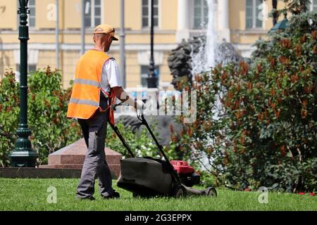 Gardener mowing the grass with lawn mower at summer. City park improvement in sunny day Stock Photo
