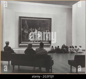 Night vandelzaal with visitors to banks and sitting on the ground, from behind; Visitors view the night watch in 1960. Zaal seen to the west. Stock Photo