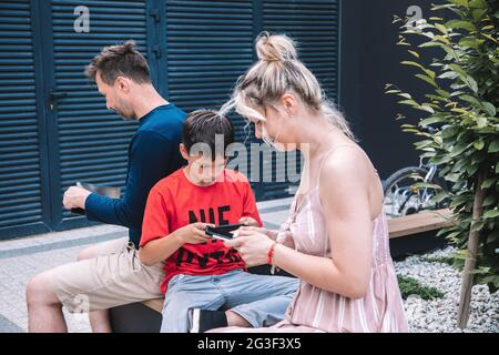 Modern young family using modern technology.On walk in the city square, everyone looks at their smartphones or tablets.They are not attracted to each Stock Photo