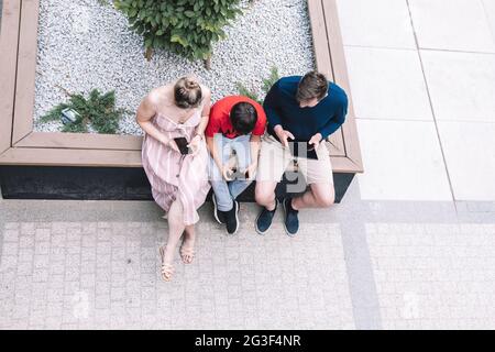 Parents and son are sitting next to each other on the street. Everyone is passionate about smartphones or tablets. They don't talk to each other.Using Stock Photo