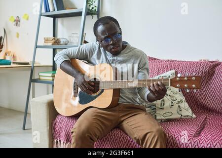 African young man sitting on sofa and playing guitar at home Stock Photo