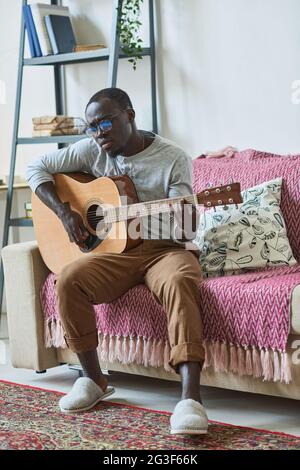 African man playing guitar while sitting on sofa in the room Stock Photo