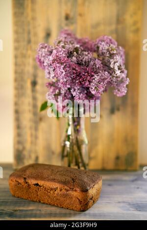 Homemade rye yeast-free bread lies on a wooden table next to a bouquet of lilacs Stock Photo