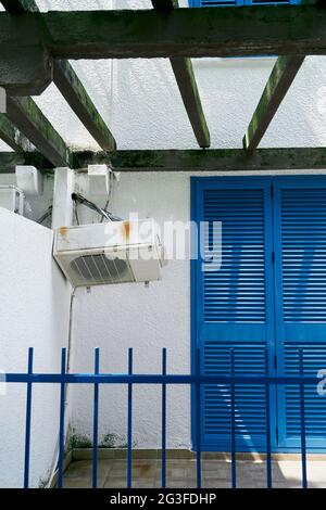 Air conditioner hangs on the white wall of the house near the blue door Stock Photo