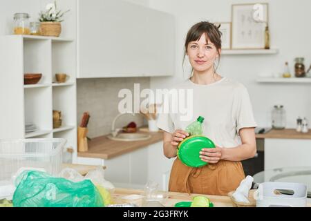 Portrait of young woman looking at camera while sorting the plastic in the kitchen Stock Photo